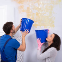 Man and woman holding blue buckets under a ceiling leak